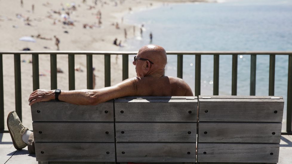 Un hombre sin camiseta observa la playa de Riazor, en A Coruña