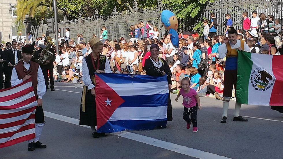Una ni�a entrega un global a las j�venes que sostienen la bandera de Cuba en el Desfile del D�a de Am�rica en Asturias.Una ni�a entrega un globo a las j�venes que sostienen la bandera de Cuba en el Desfile del D�a de Am�rica en Asturias