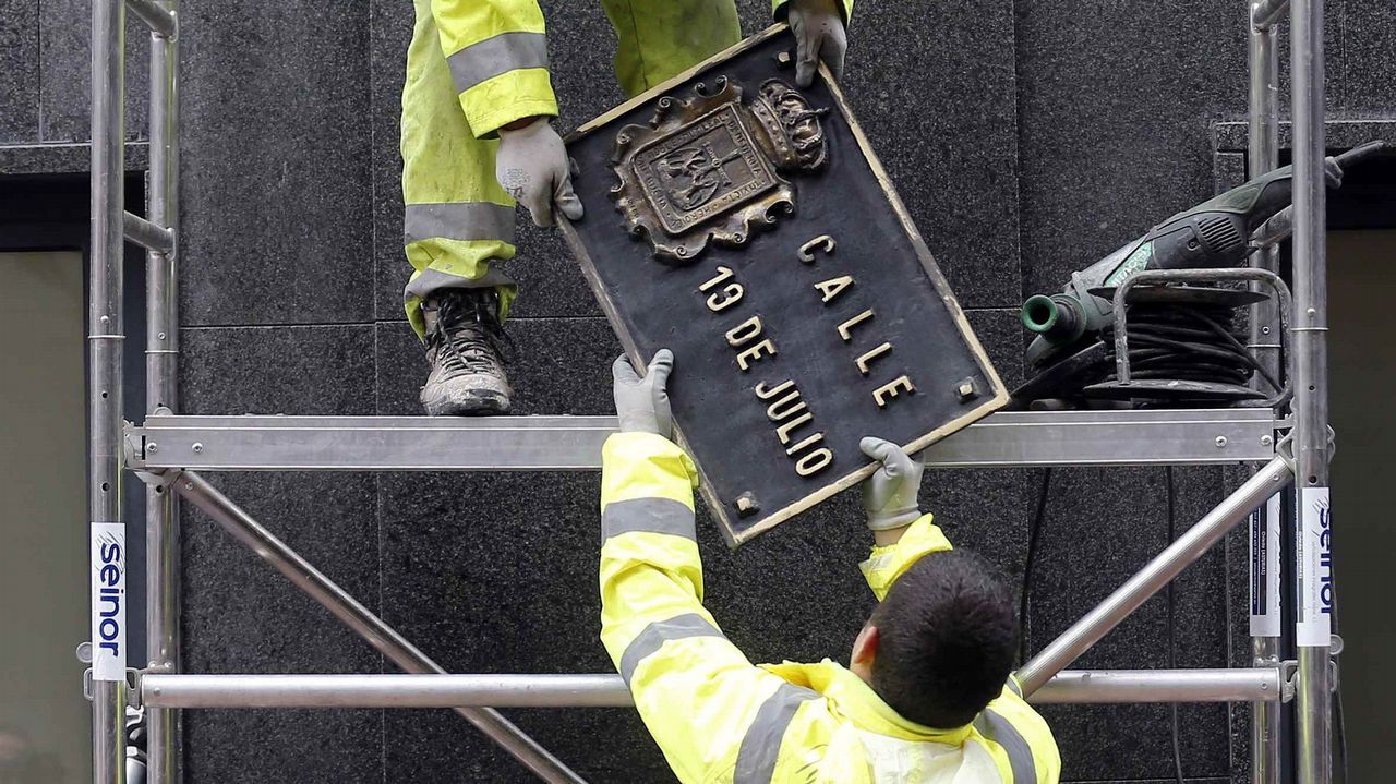 Dos operarios trabajan en la sustitución de la placa de la calle 19 de Julio, en el centro de Oviedo, en aplicación de la ley de Memoria Histórica por parte del Ayuntamiento de Oviedo