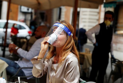 Un camarero, con guantes y mascarilla, sirve un café a un cliente, esta mañana en una plaza de Roma