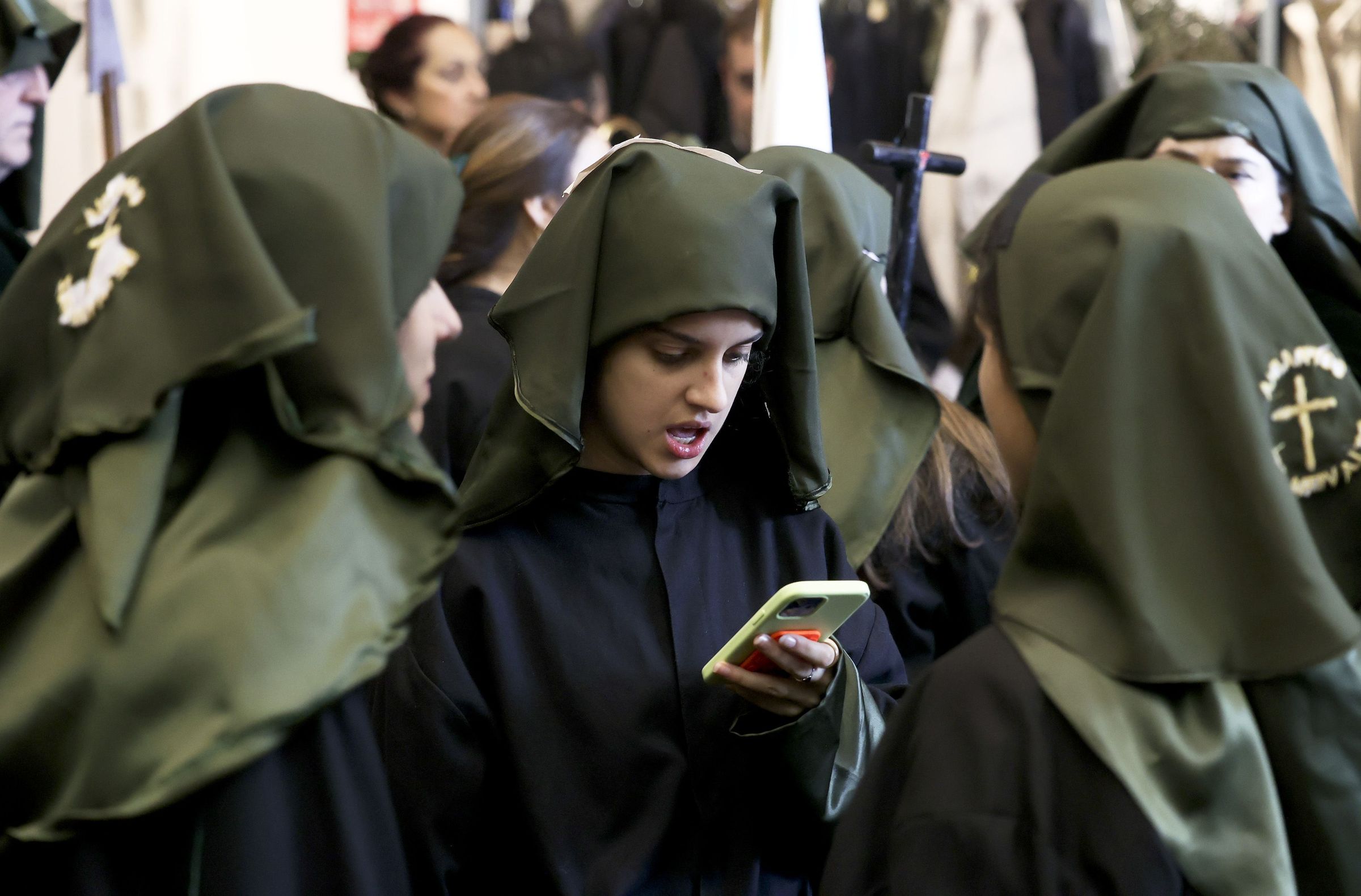 Xvenes nazarenos miran o mbil  espera de saber si vai sair a procesin do Cristo Resucitado. 20/04/2025