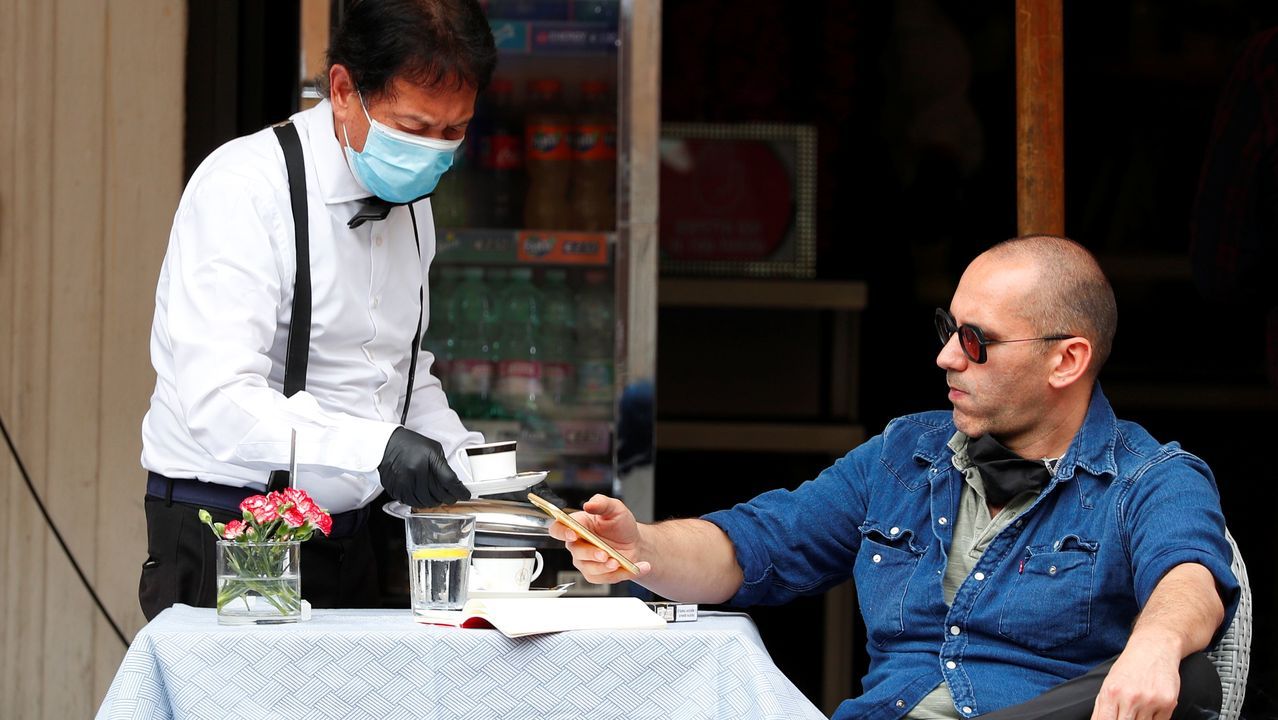 Un camarero, con guantes y mascarilla, sirve un café a un cliente, esta mañana en una plaza de Roma
