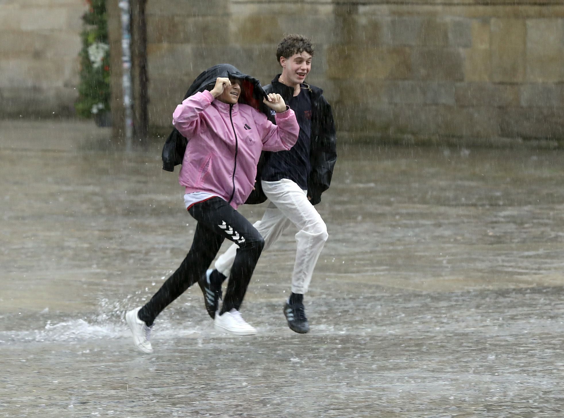 Dous mozos atravesan correndo a praza do Obradoiro baixo a choiva durante unha treboada. 30/05/2023