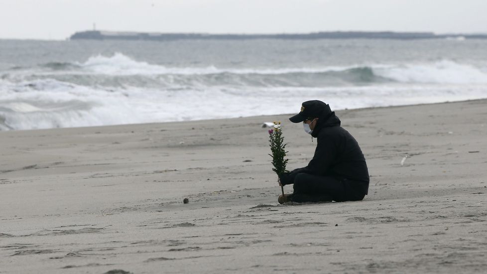 Un hombre sostiene un ramo de flores ante el mar en memoria de las víctimas.