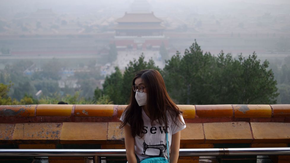 Una mujer con mascarilla posa para una foto con la Ciudad Prohibida entre una niebla de contaminación.