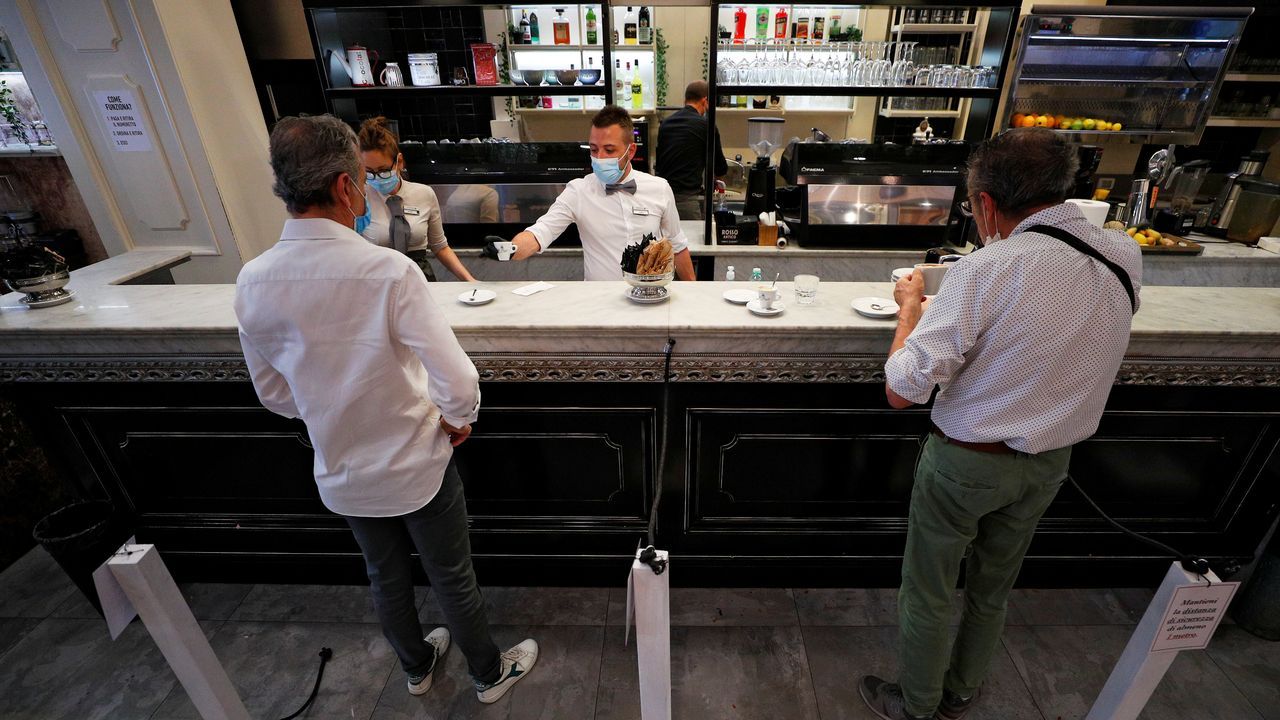 Un camarero, con guantes y mascarilla, sirve un café a un cliente, esta mañana en una plaza de Roma
