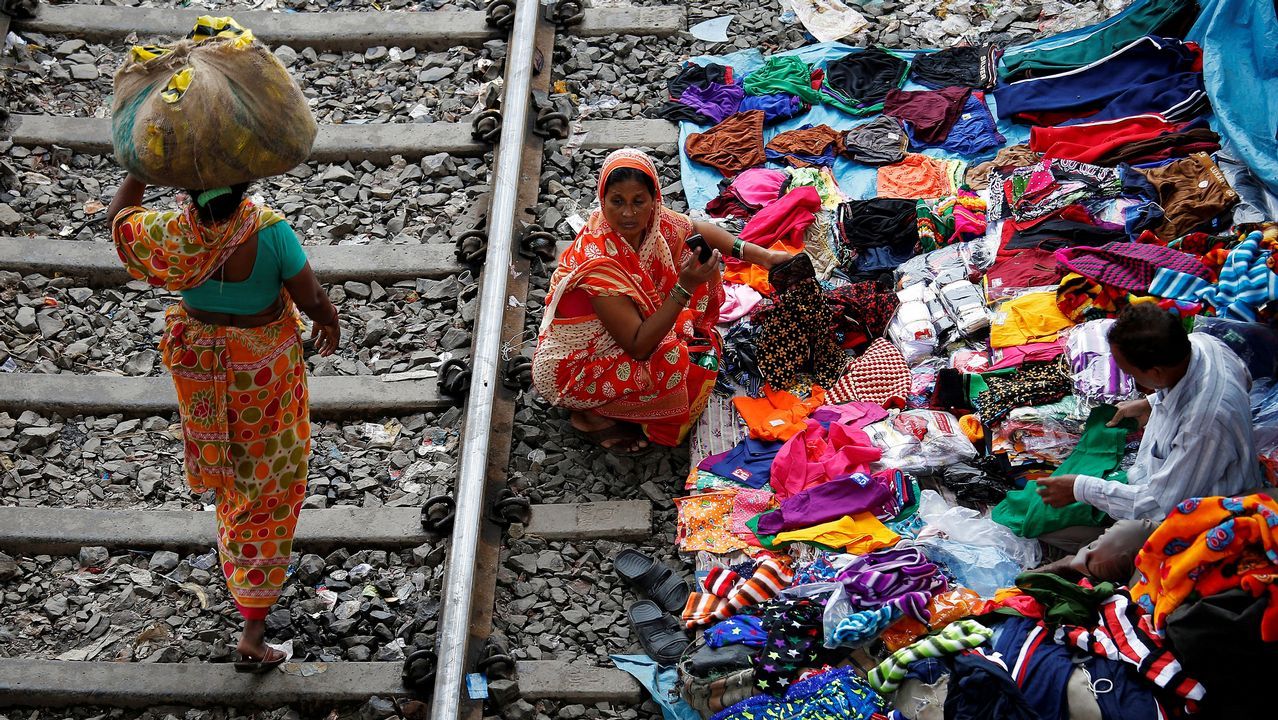 .Varias mujeres compran en un puesto improvisado en los aledaños a una vía del tren en India.