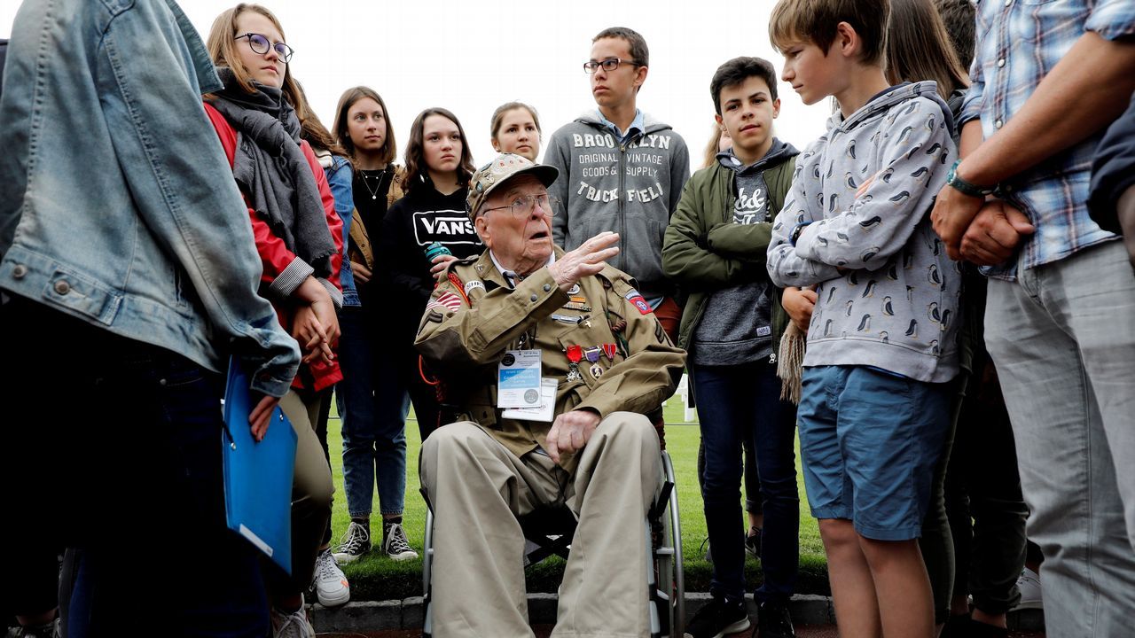 El veterano militar estadounidense George Shenkle conversa con varios jóvenes en el cementerio de los soldados caídos estadounidenses en Colleville-Sur-Mer