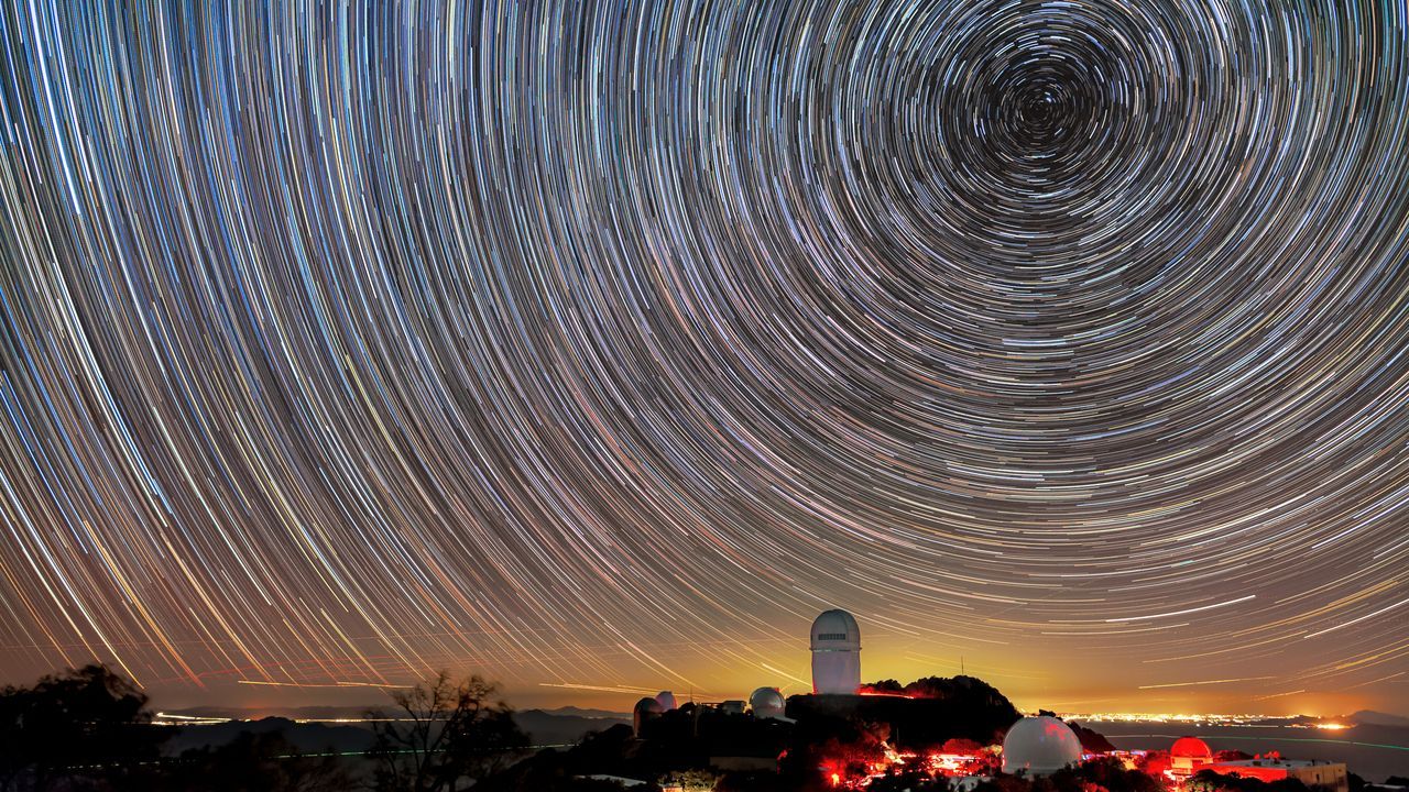 DESI cartograf�a objetos muy distantes para estudiar la energ�a oscura. El instrumento est� instalado en el telescopio Mayall, que se muestra en esta imagen bajo las estelas de las estrellas.